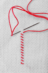 Embroidery stitches made of red thread and sewing needle on white fabric
