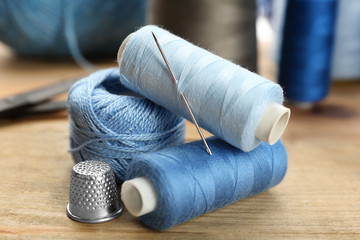 Threads and sewing needle on wooden table, closeup