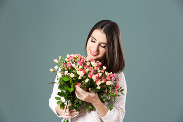 Young smiling woman with flowers on color background