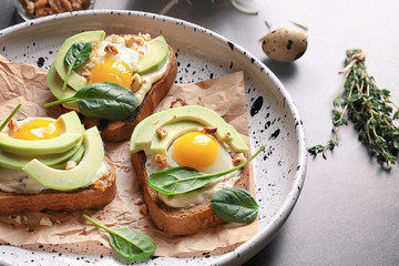 Tasty bruschettas with fried eggs and avocado on plate, closeup