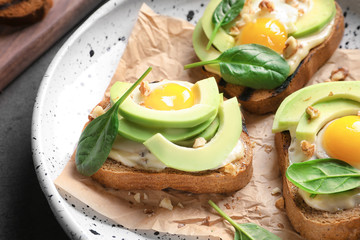 Tasty bruschettas with fried eggs and avocado on plate, closeup
