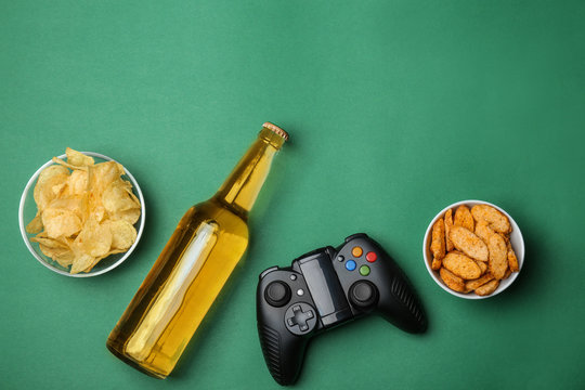 Composition with video game controller, beer and snack on color background