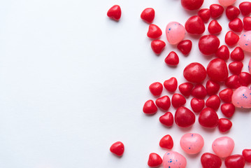 Scattered Valentine's Day cinnamon heart candies with red and pink jelly beans on white background