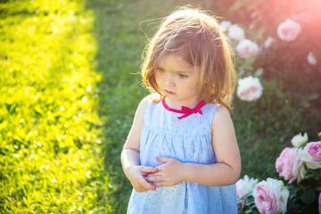 Child with thinking face in blue dress at blossoming roses