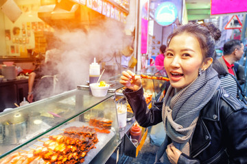 Asian young womanl eating Grilled octopus on a street in Hong Kong