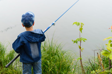 A fisherman boy on the river bank with a fishing rod in his hands. He wants to catch a big fish..