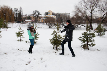 A guy and a girl are playing snowballs in a city park