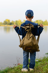 The boy on the river bank is traveling. He came by bicycle. He looks at the watery surface..