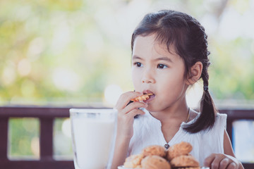 Cute asian little child girl eating cookie with milk for breakfast with happiness