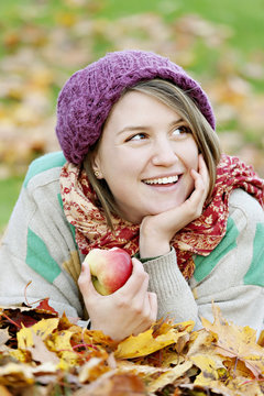 Cheerful teenage girl lying on autumn leaves with apple