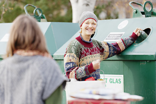 Young cheerful woman with bucket selecting rubbish while throwing them into recycle bin