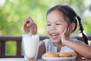 Cute asian little child girl eating cookie with milk for breakfast with happiness