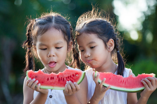 Two Cute Asian Little Child Girls Eating Watermelon Fresh Fruit In The Garden Together