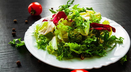 various fresh mix salad leaves with lettuce, radicchio, and rocket in plate on dark wooden background
