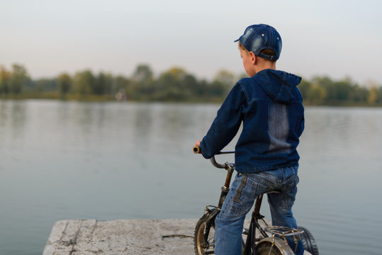 The boy on the river bank is traveling. He came by bicycle. He looks at the watery surface..