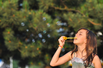 Cute girl blowing soap bubbles in summer park. Little girl play in park and blowing soap bubbles