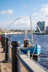 Quayside along Tyne River, in Newcastle. With blurred image of boat and Gateshead Millennium Bridge on background .