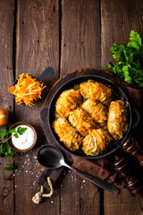 Cabbage rolls stewed with meat and vegetables in pan on dark wooden background, top view