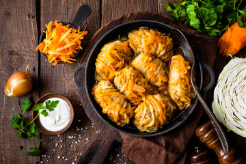 Cabbage rolls stewed with meat and vegetables in pan on dark wooden background, top view