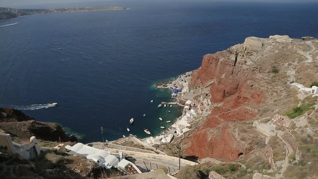 White houses lying on top of mountain on Santorini, bay at bottom of red cliff