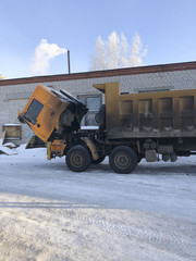 A large career dirty truck got up for winter repairs on the street. The cabin  dump truck is pushed forward to repair the engine.