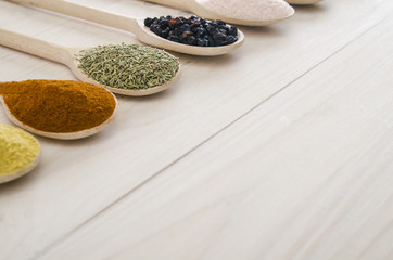 different spices in wooden spoons on a white wooden background