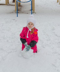 a girl sculpts a snowman in the Playground in winter