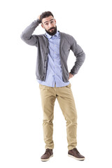 Confused young bearded stylish casual man with hand in hair looking at camera. Full body length...