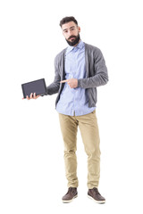 Confident bearded stylish business man pointing at blank pad tablet computer screen. Full body length portrait isolated on white studio background. 