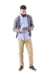 Young adult bearded hipster holding and watching at tablet computer. Full body length portrait isolated on white studio background. 