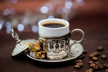 Traditional Turkish coffee in traditional metal cup on brown background with Turkish delight and bokeh