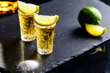 Gold Mexican tequila with lime and salt on dark table