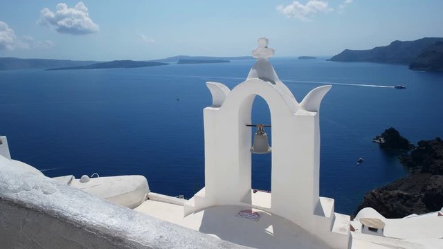 whitewashed church bell arch and blue water in the caldera at oia on the island of santorini, greece