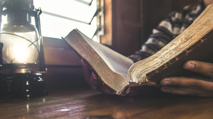Hands of young man praying and reading Bible at home