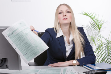 Junge Geschäftsfrau sitzt genervt mit Steuerformularen am Schreibtisch