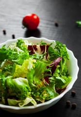 various fresh mix salad leaves with lettuce, radicchio, and rocket in bowl on dark wooden background