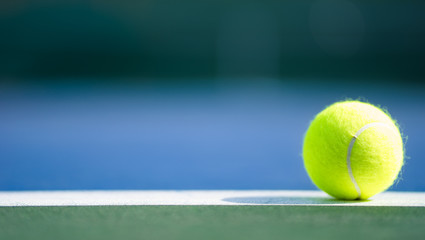 one new tennis ball on white line in blue and green hard court with light from right, shadow and...