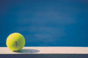 one new tennis ball on white line in blue hard court with light from left, shadow and copy space on right, vintage tone