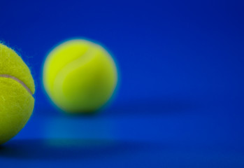 two new tennis balls on blue court with light from left, shadow and copy space on right