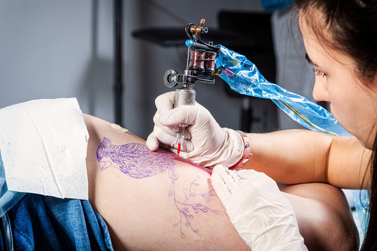 Close up of the tattooist making by professional artist is tattooing body woman using machine in a creative design work studio