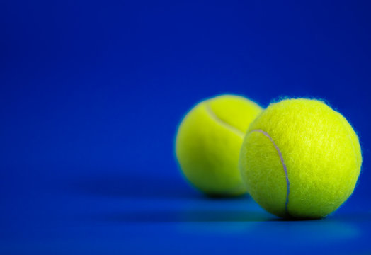 two new tennis balls on blue court with light from right, shadow and copy space on left