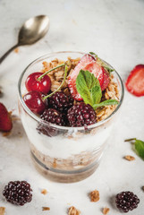 Healthy breakfast. Summer berries and fruits. Homemade Greek yoghurt with granola, blackberries, strawberries, cherries and mint. On white concrete stone table, in glasses. Copy space close view
