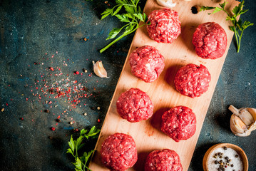 Raw meatballs with olive oil and spices on dark concrete table, top view copy space