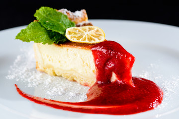 Delicious cheesecake with jam, citrus, mint and powdered sugar on the plate and on dark background, close-up