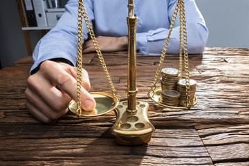 Businessperson Balancing Coins On Justice Scale With His Finger