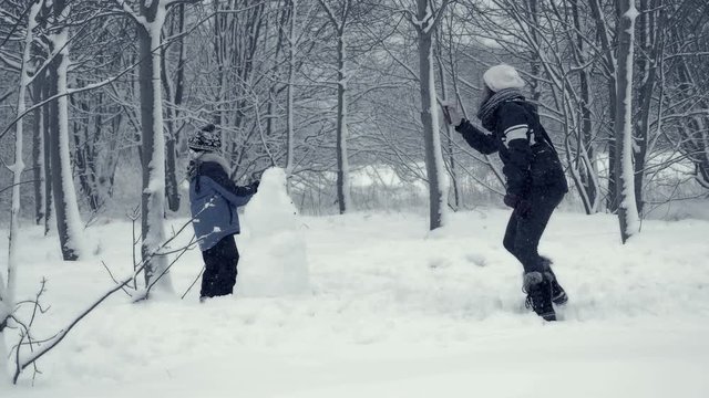 Mother and son build snowman. Family plays in snow. People enjoy winter fun. Winter landscape with child and falling snow. Everything is covered with fresh powder. Winter background, Christmas theme