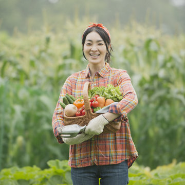 農園で野菜を持ち微笑む女性