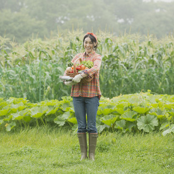 農園で野菜を持ち微笑む女性
