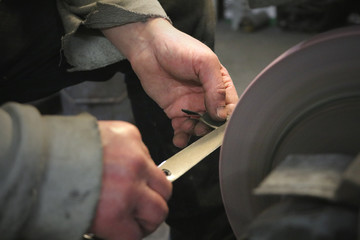 Man sharpening scissors at a whetstone in a grindery