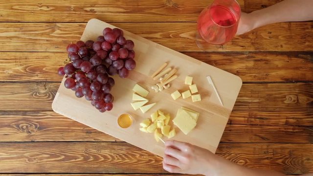 Woman with red wine eating cheese. Grapes and cheese on a wooden table.